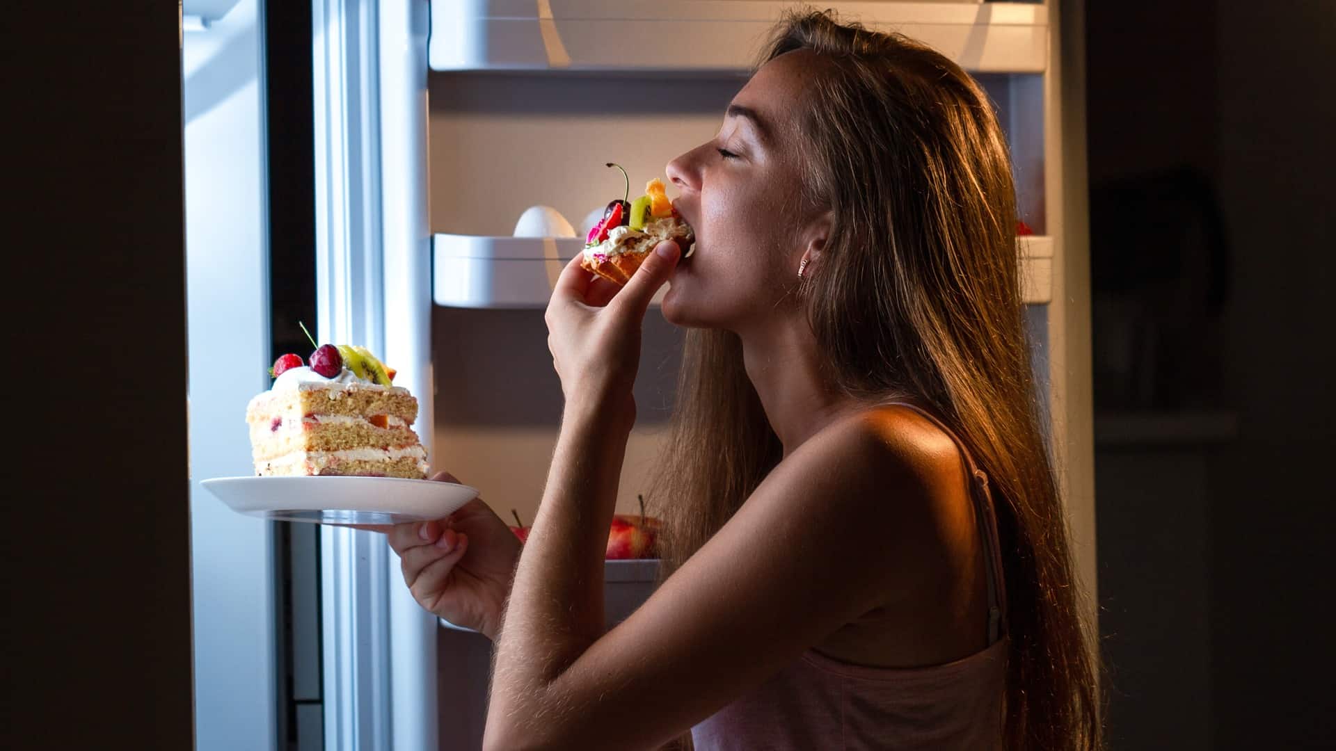 woman eating cake from the fridge